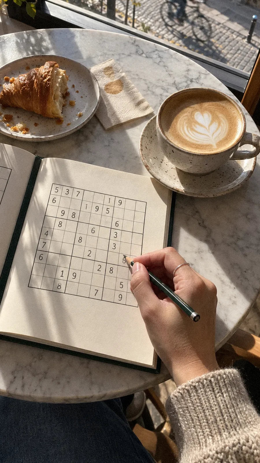 Sudoku, flat white i rogalik na marmurowym stoliku w kawiarni